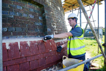 Photograph of a younger tradesman learning how to restore heritage buildings