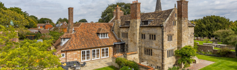 Aerial view of a historic English manor house, showcasing the stone masonry, classic architecture, and surrounding green gardens.