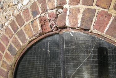 Photograph showing arched brickwork around a window needing repair.